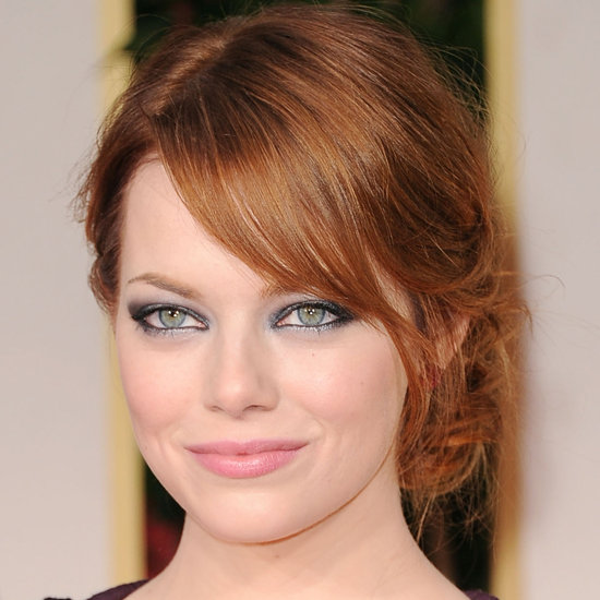 Emma Stone half smiling at the camera. Her red hair is in a bun. She is rocking the smoky eye.