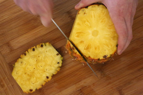 Run the knife down the length of the pineapple. You want to cut in deep enough so that all the prickly brown bits are cut off. I make about seven cuts, but you could do more or less, depending on how much you chop off, and how big your pineapple is.
Run the knife down the length of the pineapple. You want to cut in deep enough so that all the prickly brown bits are cut off. I make about seven cuts, but you could do more or less, depending on how much you chop off, and how big your pineapple is.