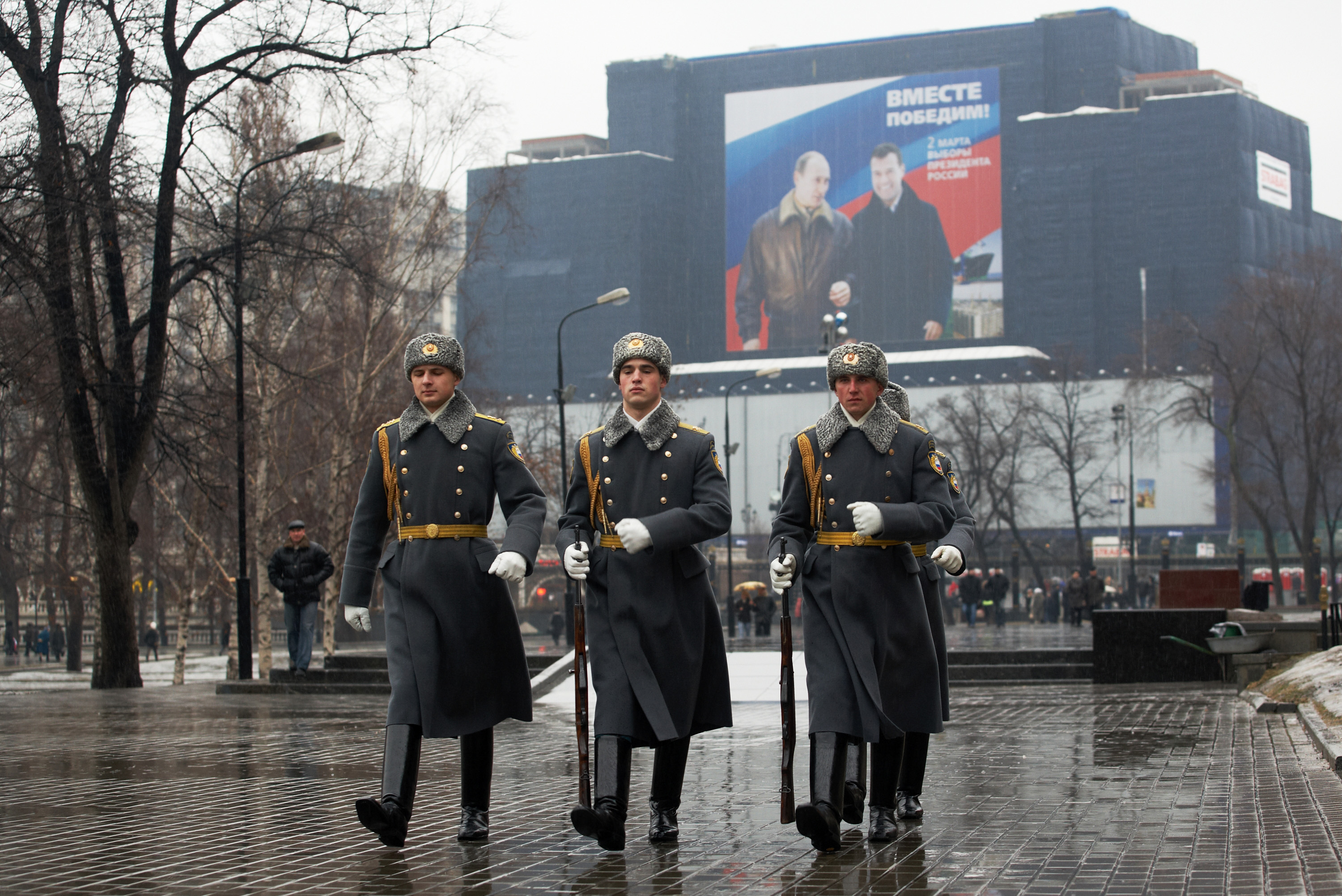 Guards of honor walk past a large election poster. Guards of honor walk past a large election poster.