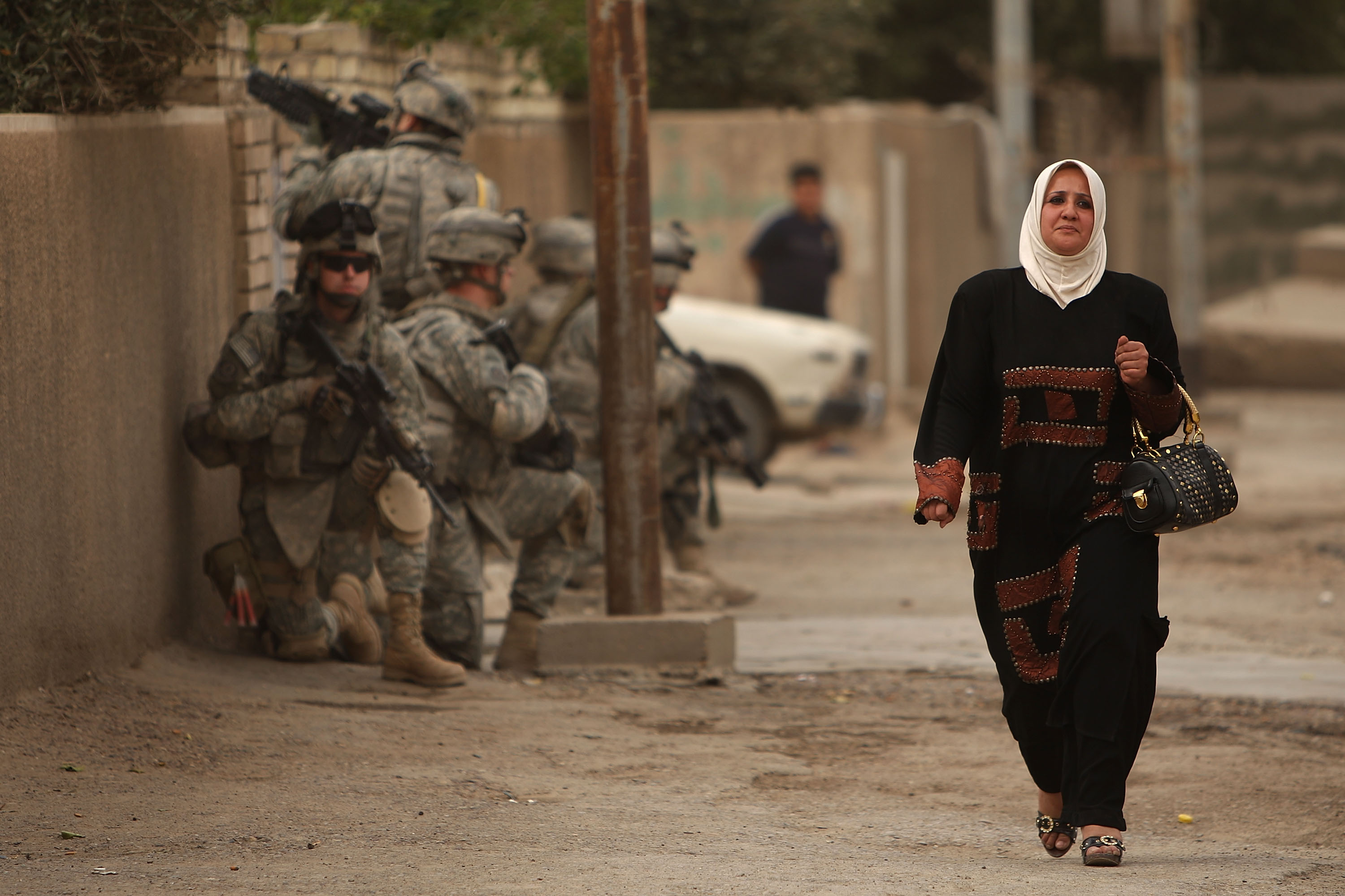 A woman walks past a group of US soldiers in the war ravaged Hadar neighborhood March 10, 2008 in Baghdad. A woman walks past a group of US soldiers in the war ravaged Hadar neighborhood March 10, 2008 in Baghdad.