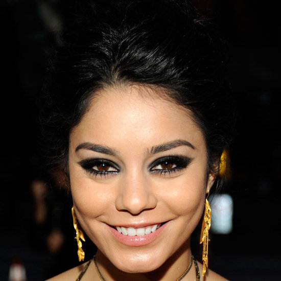 Vanessa Hudgens smiling directly at the camera. She is wearing gold chandelier earrings. Her hair is up. She is rocking the smoky eye look.